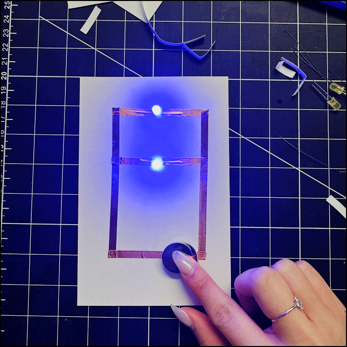 Image of completed parallel circuit with 2 batteries pressed down by the positive side of the circuit (copper tape)